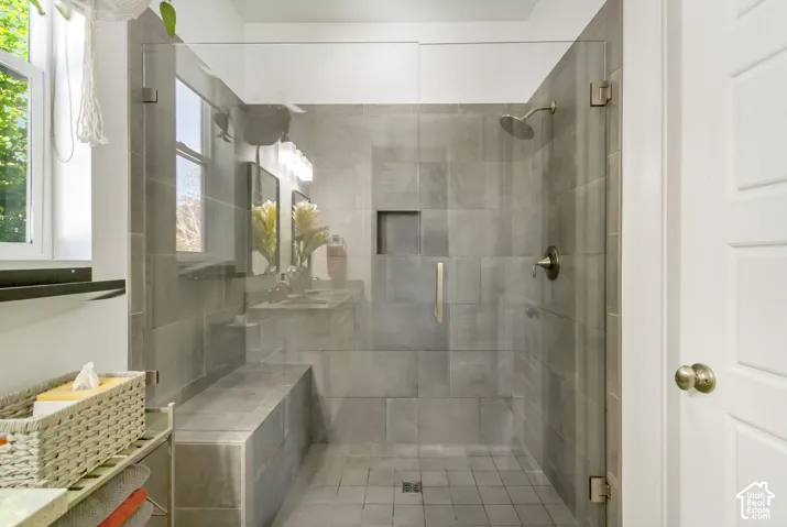 Walk-in shower featuring large-format grey tile surround, built-in tile bench, glass door, recessed wall niche, and metal finish fixtures