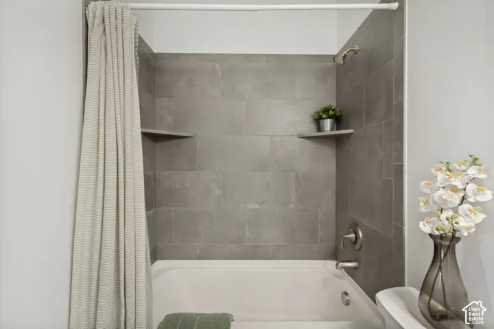 Bathtub shower combination featuring grey rectangular tile surround, two integrated corner shelves, and brushed metal fixtures