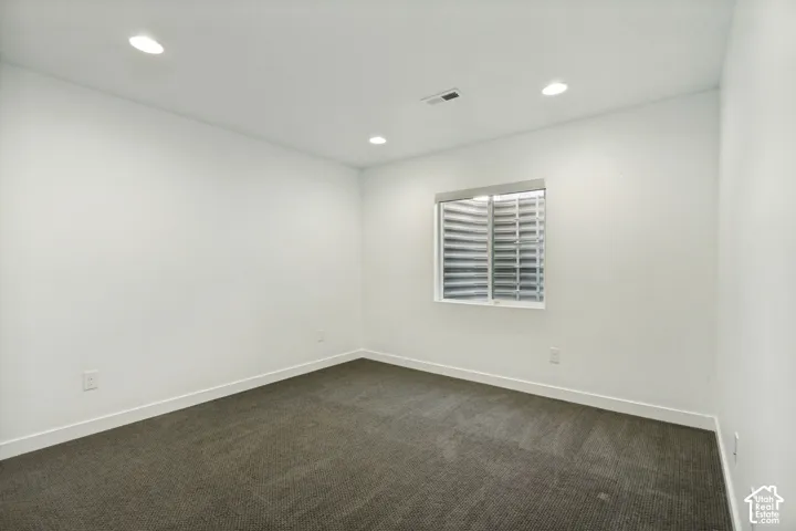 Neutral-toned interior space featuring recessed ceiling lighting, wall-to-wall carpeting, and a window with an egress well