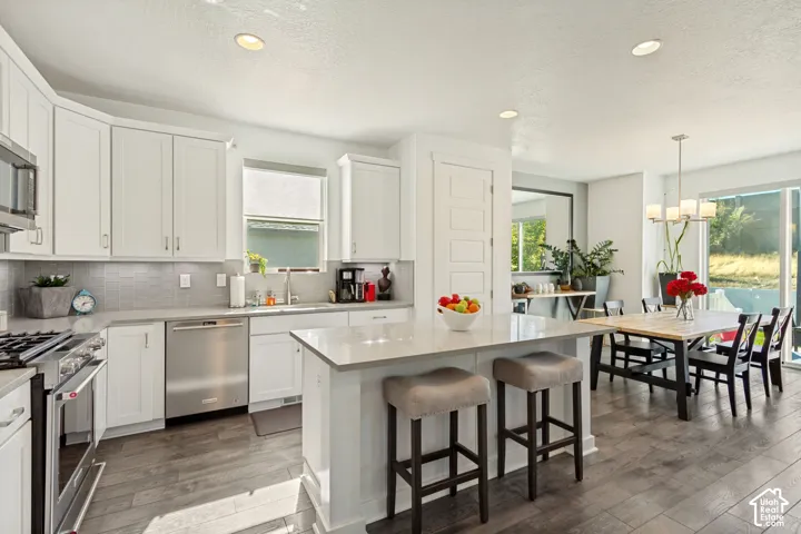 Kitchen featuring white shaker-style cabinetry, a quartz-topped center island, stainless steel appliances, a tiled backsplash, and wood-finish flooring