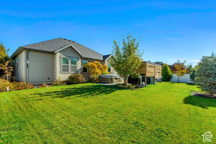 Rear exterior featuring a manicured lawn, wood-slat privacy screen, built-in hot tub, and mature landscaping enclosed by white vinyl fencing