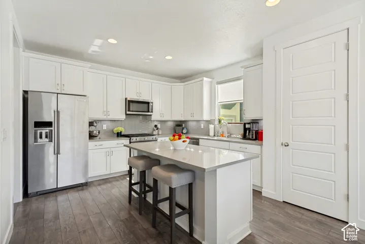Kitchen featuring white shaker-style cabinetry, quartz countertops, a central island, stainless steel appliances, and wood-finish flooring