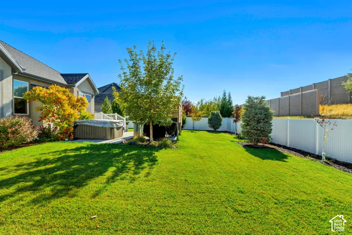Backyard featuring a manicured lawn, white vinyl privacy fencing, integrated hot tub, and established landscaping