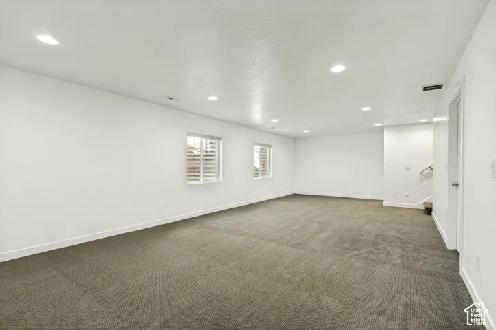 Open-concept interior featuring neutral carpeting, recessed ceiling lighting, and two egress-style windows