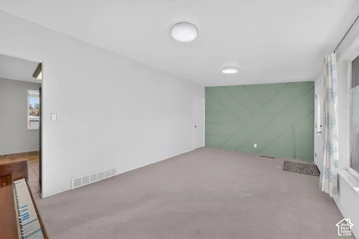Interior space featuring a sage green accent wall with geometric wood trim, neutral carpeting, and dual flush-mount ceiling light fixtures