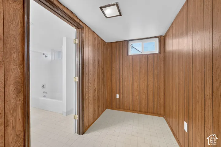 Wood-paneled walls, tile flooring, built-in ceiling lighting, a sliding egress window, and a white tile surround bathtub