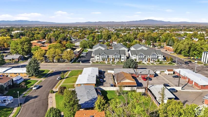 Aerial perspective of the neighborhood featuring paved streets, established tree canopy, multi-unit residential structures, and distant mountain scenery