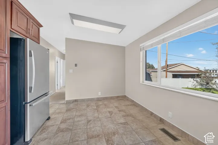 Kitchen featuring cherry-finish cabinetry, stainless steel refrigerator, neutral tile flooring, and large window with exterior exposure