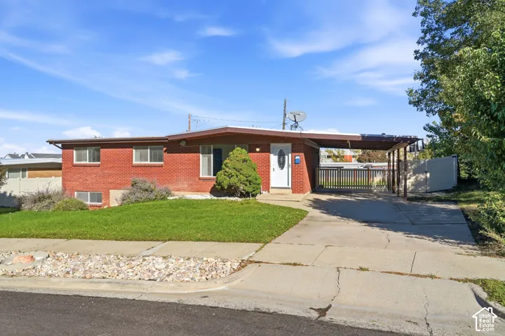 Mid-century inspired red brick exterior featuring a low-slope roofline, attached carport, concrete driveway, and white front door with an oval glass insert