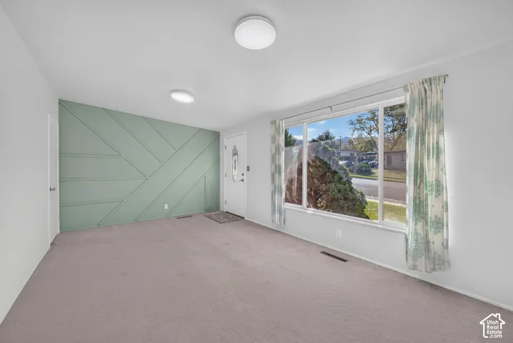 Interior space featuring a sage green geometric accent wall, carpeted flooring, large picture window, and a paneled entry door with an oval glass insert