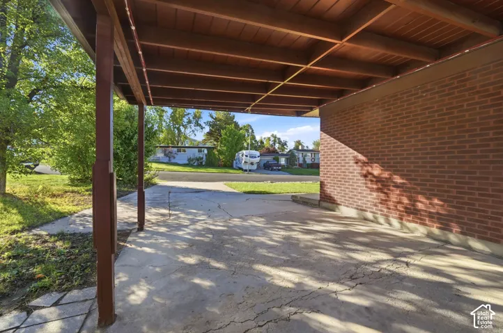 Covered carport featuring a brick exterior wall and exposed wood-beam ceiling