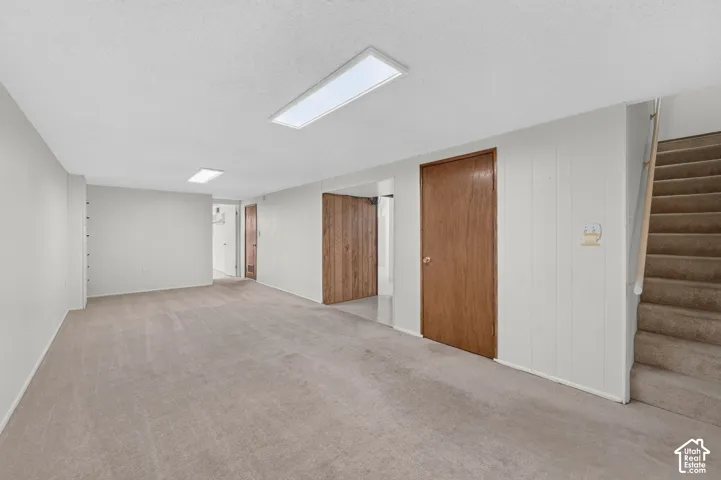 Interior space featuring neutral-toned carpeting, wood-finish paneled accents, recessed lighting, and a staircase with wall-mounted handrail