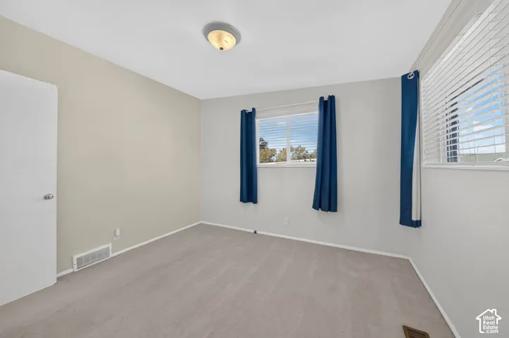 Interior room featuring neutral wall tones, wall-to-wall carpeting, two windows with horizontal blinds, and a semi-flush mount ceiling fixture