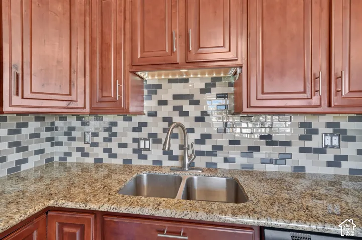 Kitchen area featuring raised-panel wood cabinetry, natural stone countertops, a dual-basin stainless steel sink with a high-arch pull-down faucet, and a multi-toned glass tile backsplash