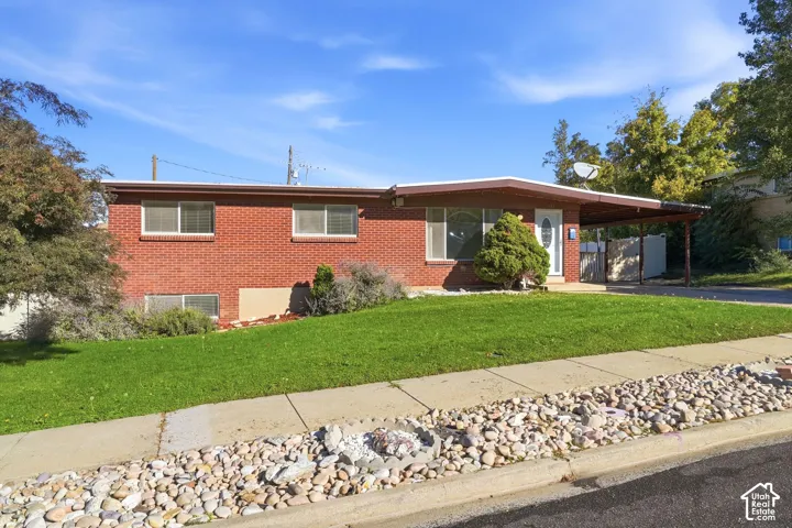 Mid-century red brick exterior featuring a low-pitch roofline, an attached covered carport, and horizontal window placements