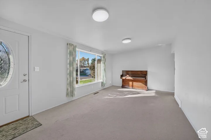Neutral interior space featuring carpeted flooring, a large picture window, and an entry door with an oval glass insert