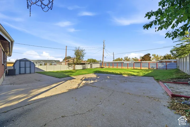Expansive backyard featuring a concrete patio, perimeter fencing, lawn area, and a detached storage structure