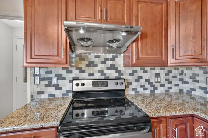 Kitchen featuring wood cabinetry, stone-surface countertops, a multicolored subway tile backsplash, a stainless steel range, and a mounted stainless steel range hood