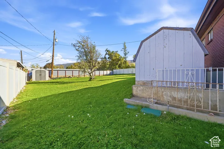 Expansive backyard featuring a fenced perimeter, mature tree, concrete retaining wall, and two detached storage structures