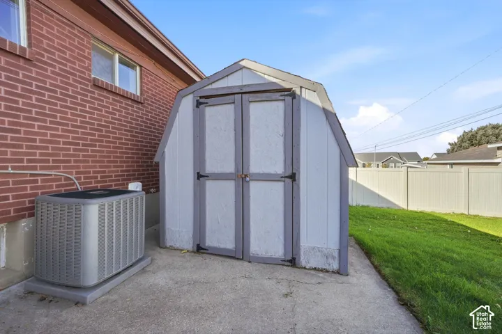 Exterior storage shed featuring a gambrel roof and double doors, situated on a concrete pad with a fenced perimeter