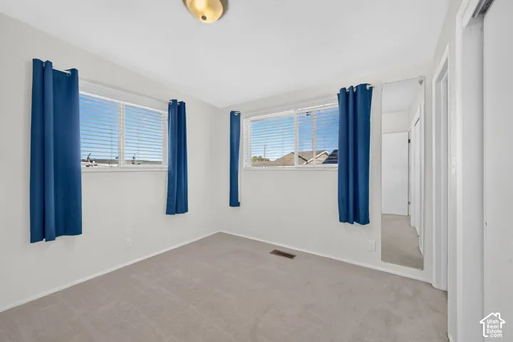 Neutral interior room featuring wall-to-wall carpeting, dual windows, and a full-length wall-mounted mirror