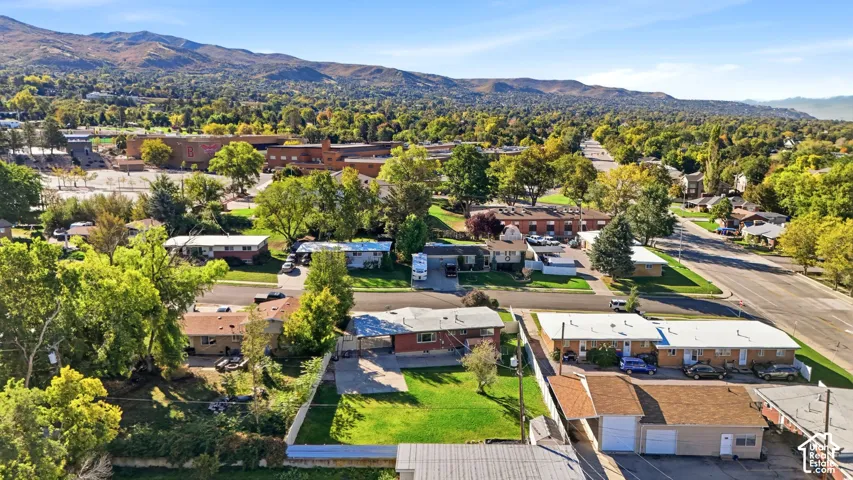 Aerial perspective of a property featuring a manicured lawn, concrete driveway, attached carport, and a detached garage, set against a backdrop of mountain ranges