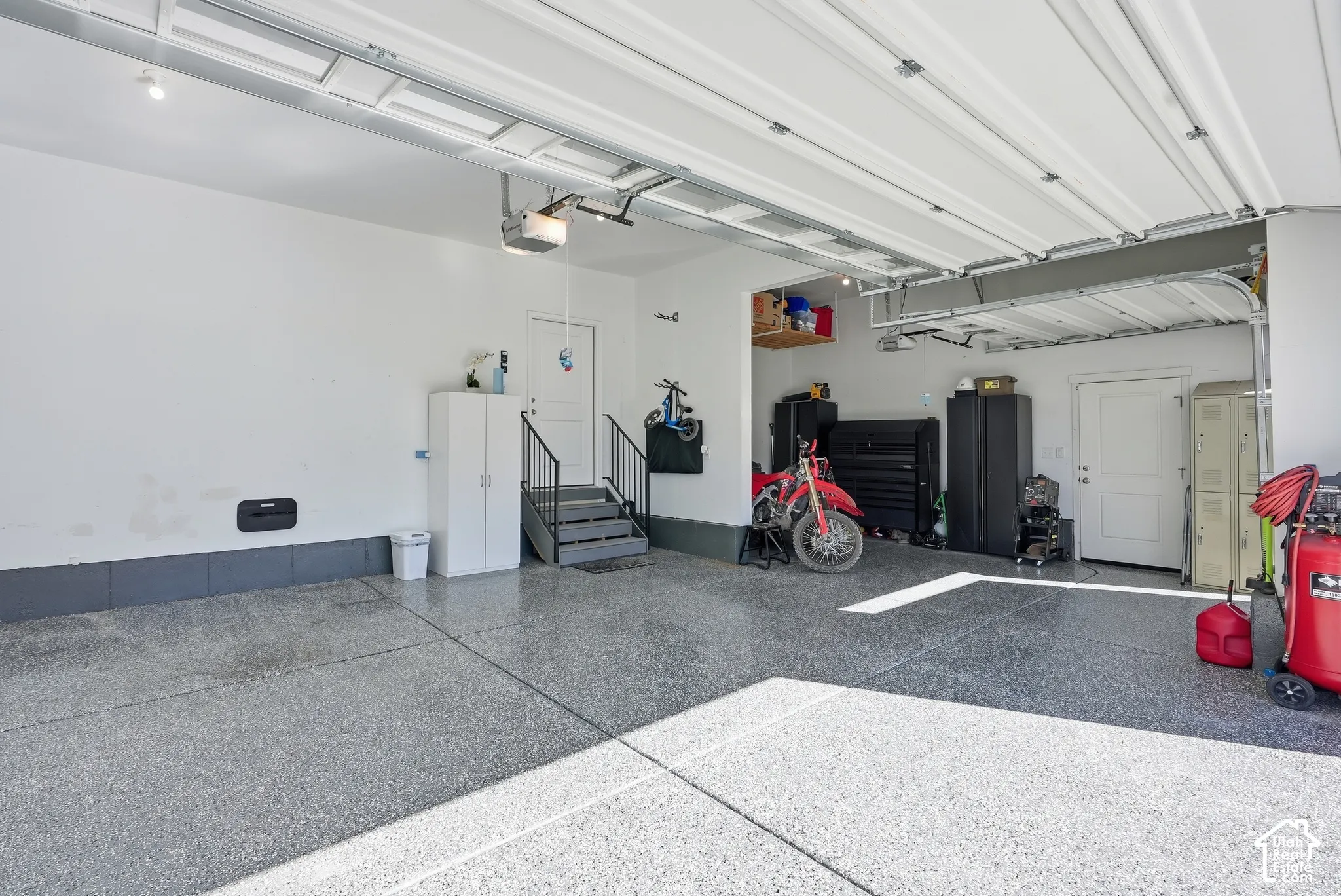 Multi-car garage featuring epoxy-finished flooring, overhead lighting, and an internal staircase with metal railings leading to an entry door