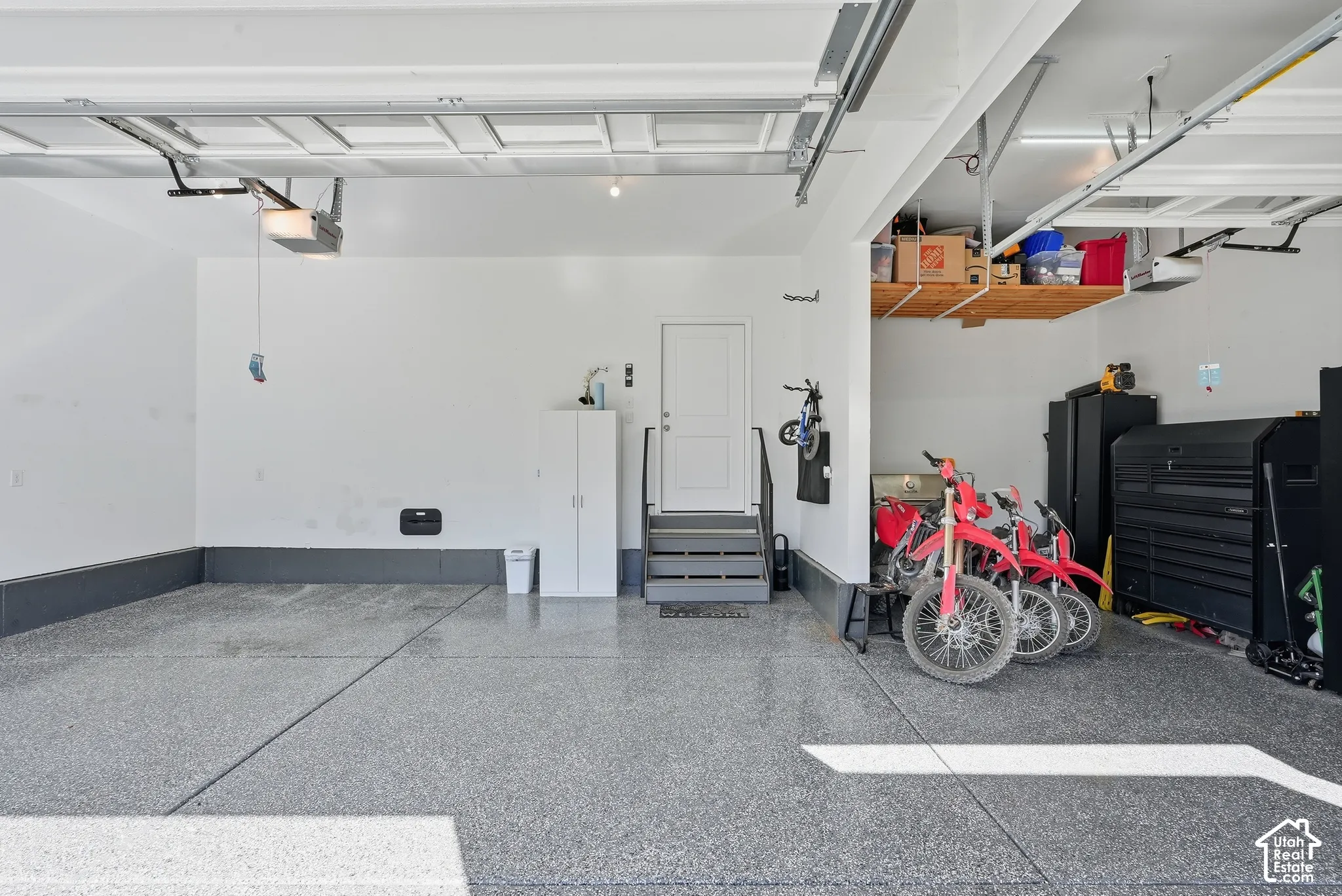 Multi-car garage featuring epoxy-coated flooring, elevated ceiling height, built-in overhead storage shelving, and a dedicated service door with an integrated staircase