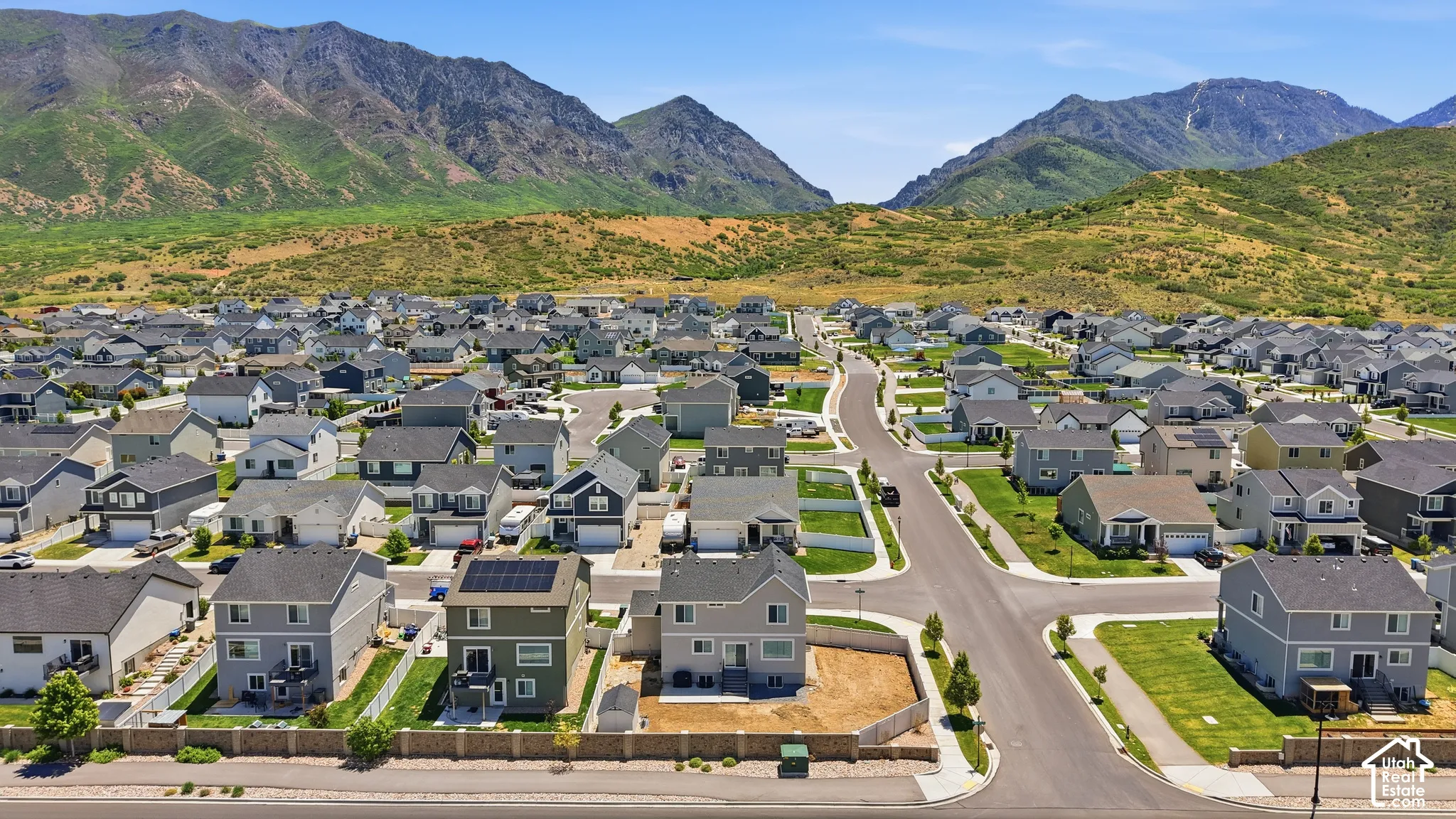 Aerial perspective showcasing multi-level residential structures, integrated solar panels, fenced perimeter hardscaping, and a prominent mountain backdrop