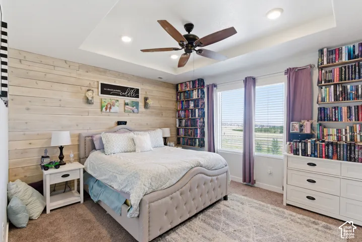 Bedroom featuring a wood-plank accent wall, tray ceiling with recessed lighting, integrated ceiling fan, and extensive built-in floor-to-ceiling shelving