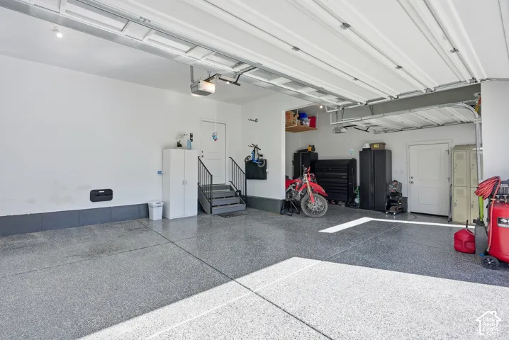 Multi-car garage featuring epoxy-finished flooring, overhead lighting, and an internal staircase with metal railings leading to an entry door