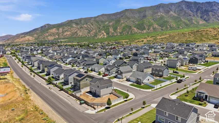 Aerial perspective featuring multi-story residential architecture, asphalt street infrastructure, vinyl fencing, solar panel installations, and a prominent mountain range backdrop