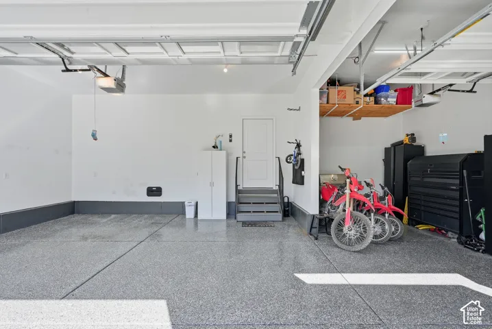 Multi-car garage featuring epoxy-coated flooring, elevated ceiling height, built-in overhead storage shelving, and a dedicated service door with an integrated staircase