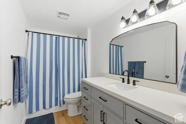Bathroom featuring a gray vanity with matte black hardware, white countertop, integrated rectangular sink, wall-mounted arched mirror, and multi-bulb vanity lighting
