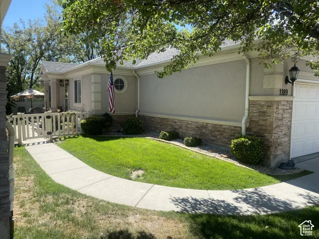 Stucco exterior facade featuring stone veneer skirting, curved concrete walkway, accent quoins, and enclosed gate entry