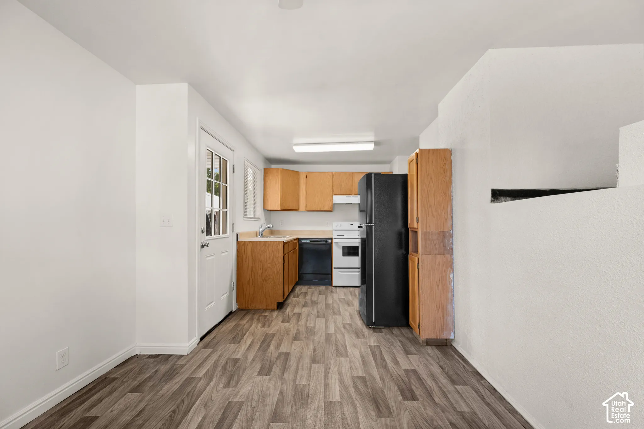 Kitchen featuring wood-finish cabinetry, hard-surface countertops, wood-finish flooring, a full-size refrigerator, and a dishwasher