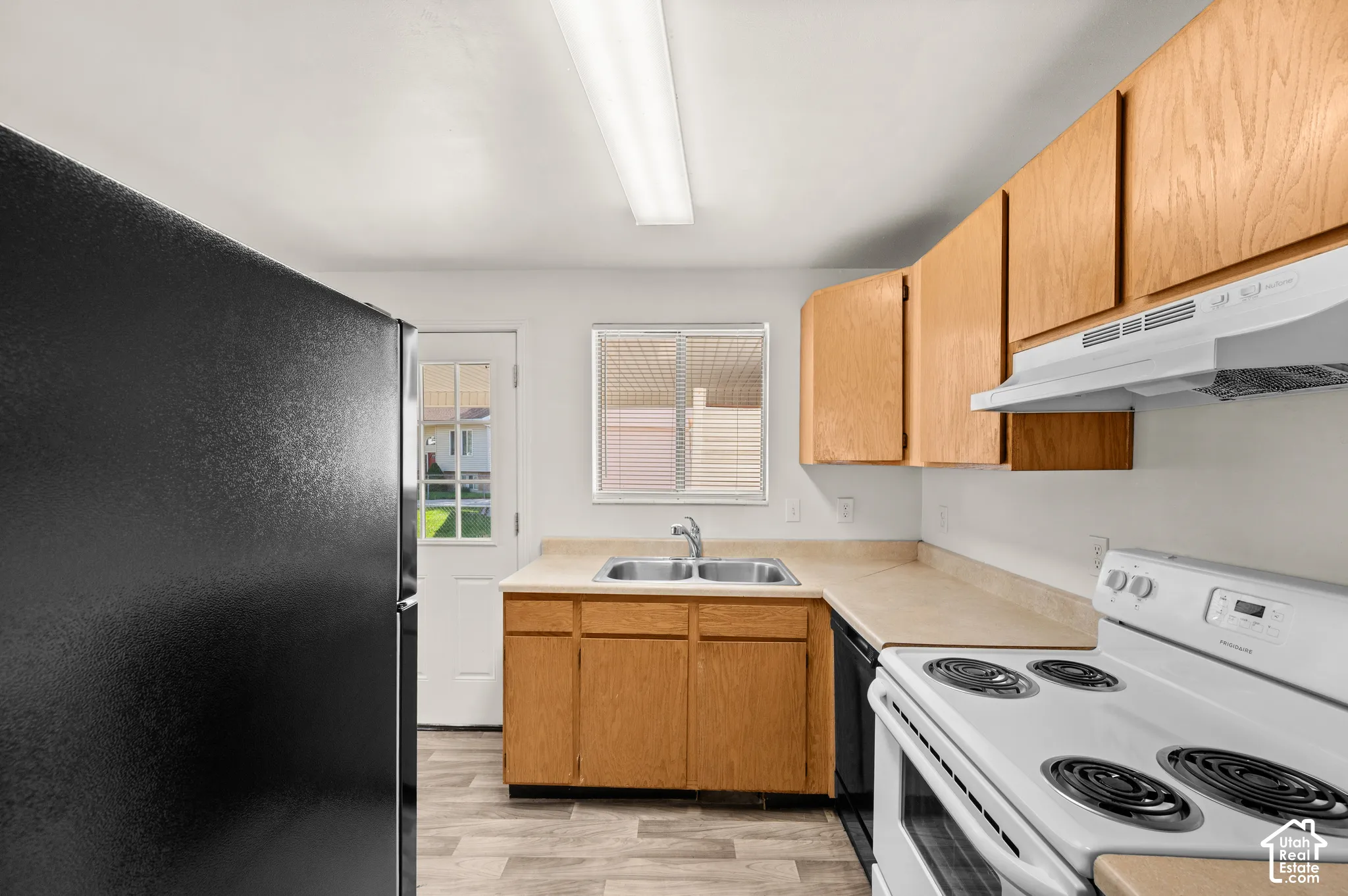 Kitchen featuring wood-finish cabinetry, solid-surface countertops, a double-basin stainless steel sink, and wood-finish flooring