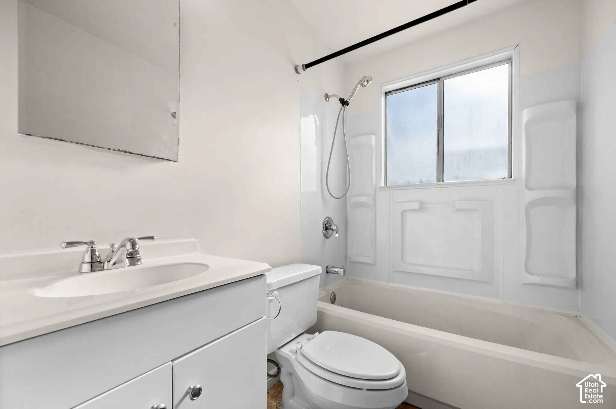 Bathroom featuring a vanity with an integrated sink and chrome faucet, a wall-mounted mirror, a porcelain toilet, and a bathtub with a shower head and white surround