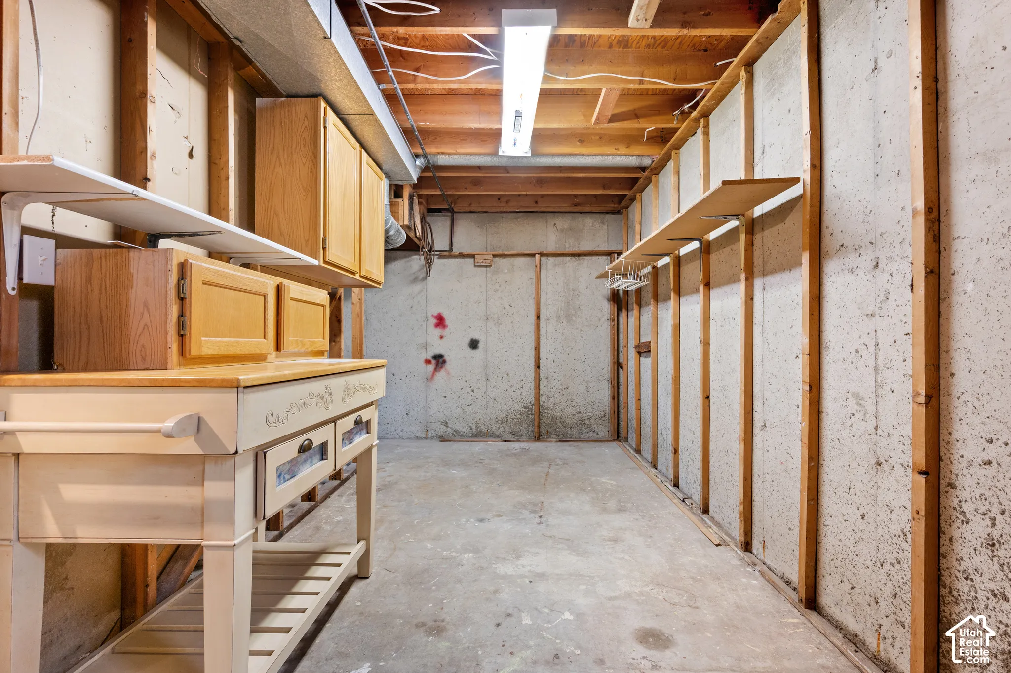Utility space featuring concrete foundation walls, exposed wood framing, linear overhead lighting, and built-in wood cabinetry