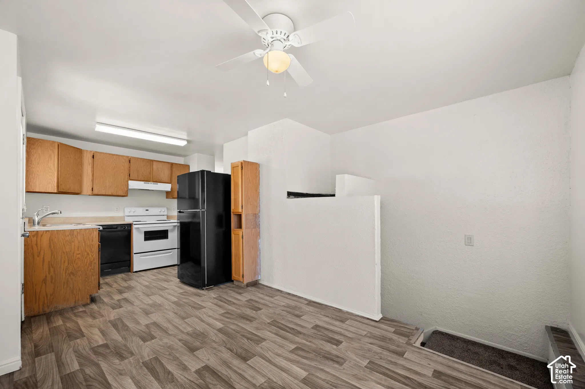 Kitchen featuring wood-finish cabinetry, solid surface countertops, a black refrigerator, a white freestanding range, and wood-finish flooring