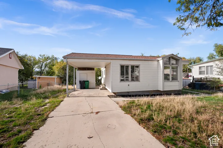 Single-story exterior featuring white horizontal siding, a covered carport, concrete driveway, and tall picture windows