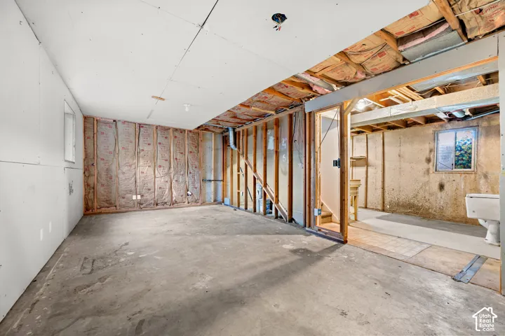 Unfinished basement area featuring concrete flooring, exposed wooden stud framing, exposed fiberglass insulation, and a single-pane window