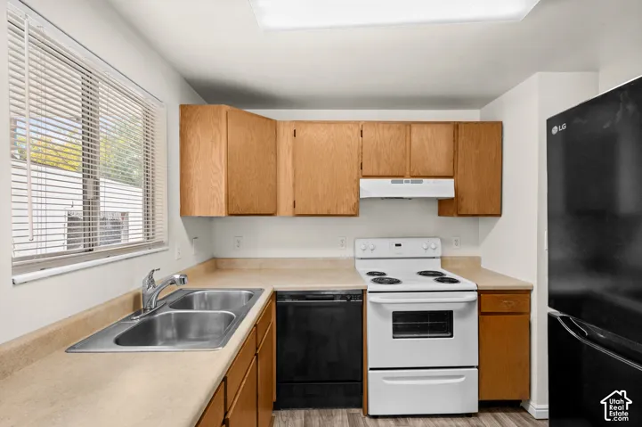 Kitchen featuring wood cabinetry, solid surface countertops, dual-basin stainless steel sink, integrated range hood, and resilient wood-finish flooring