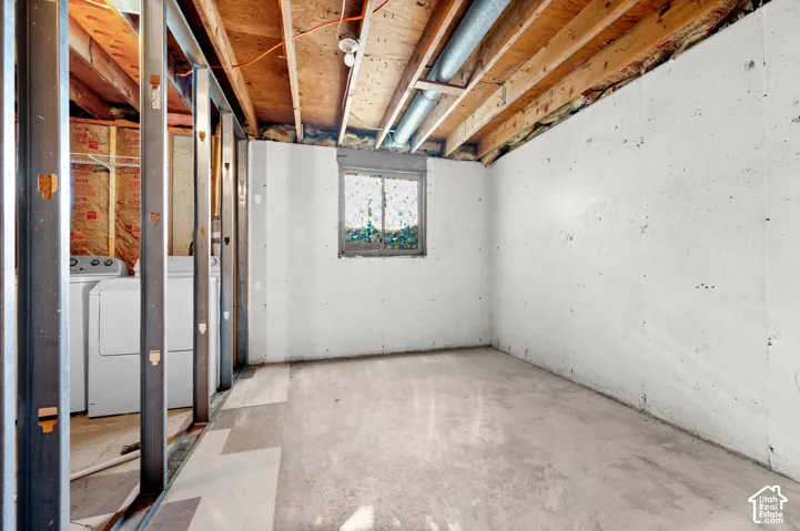 Unfinished lower-level space featuring concrete walls, exposed ceiling joists, metal stud framing, and a window