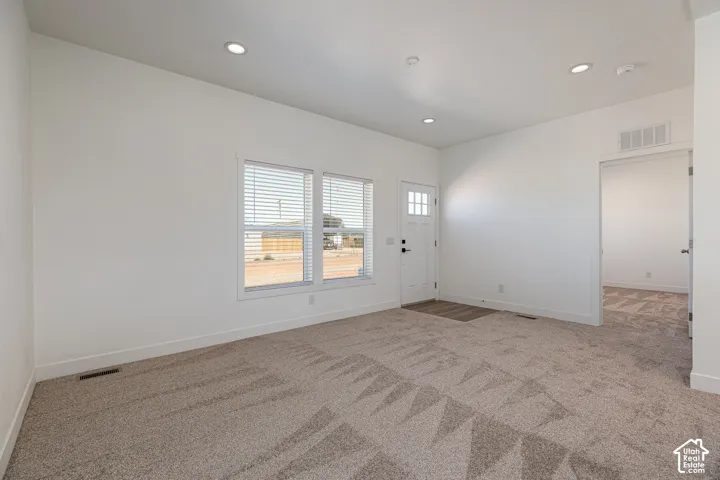 Neutral-toned interior space featuring recessed ceiling lighting, wall-to-wall carpeting, dual-pane windows with horizontal blinds, and a paneled exterior door with glass detailing
