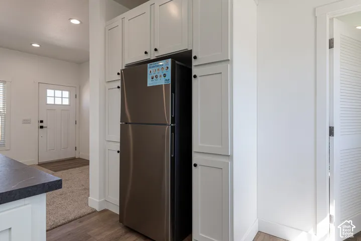 Floor-to-ceiling white cabinetry featuring integrated refrigeration storage, recessed ceiling lighting, and wood-finish flooring