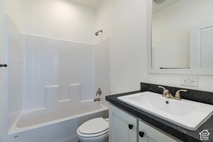 Bathroom featuring a white composite tub and shower surround, dark countertop with an integrated basin, white cabinetry with dark hardware, and a framed mirror