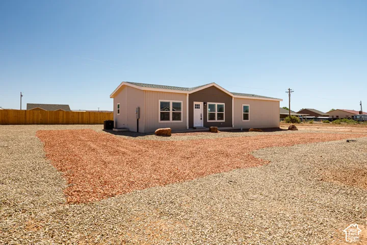 Single-story exterior featuring a dual-tone siding facade, shingle roof, multi-pane windows, and a gravel-surfaced lot with decorative stone elements
