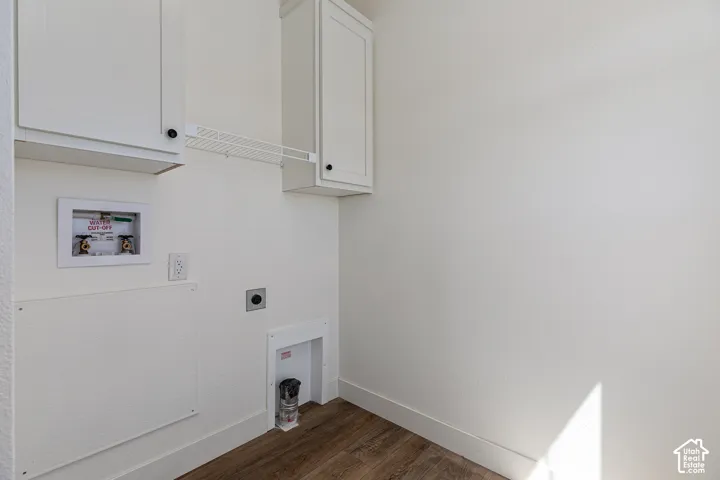 Utility space featuring wood-finish flooring, white shaker-style cabinetry, a wire shelving unit, and recessed plumbing connections