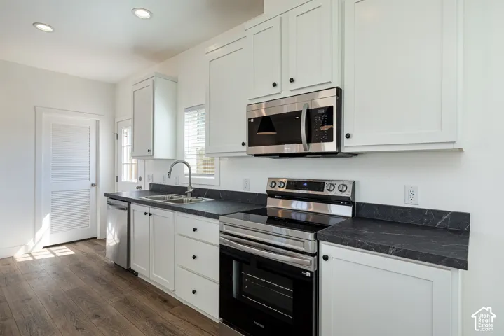 Kitchen featuring white shaker-style cabinetry, dark stone-finish countertops, stainless steel appliances, recessed lighting, and wood-finish flooring